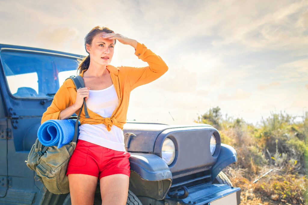 Woman leaning against jeep with yoga mat.